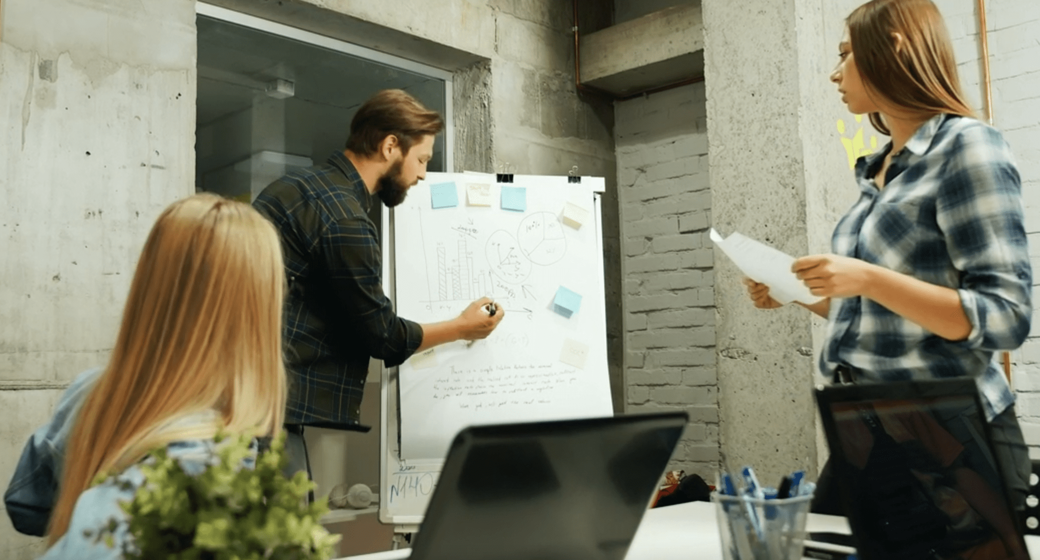 three people looking at a standing up board with graphs drawn on it.
